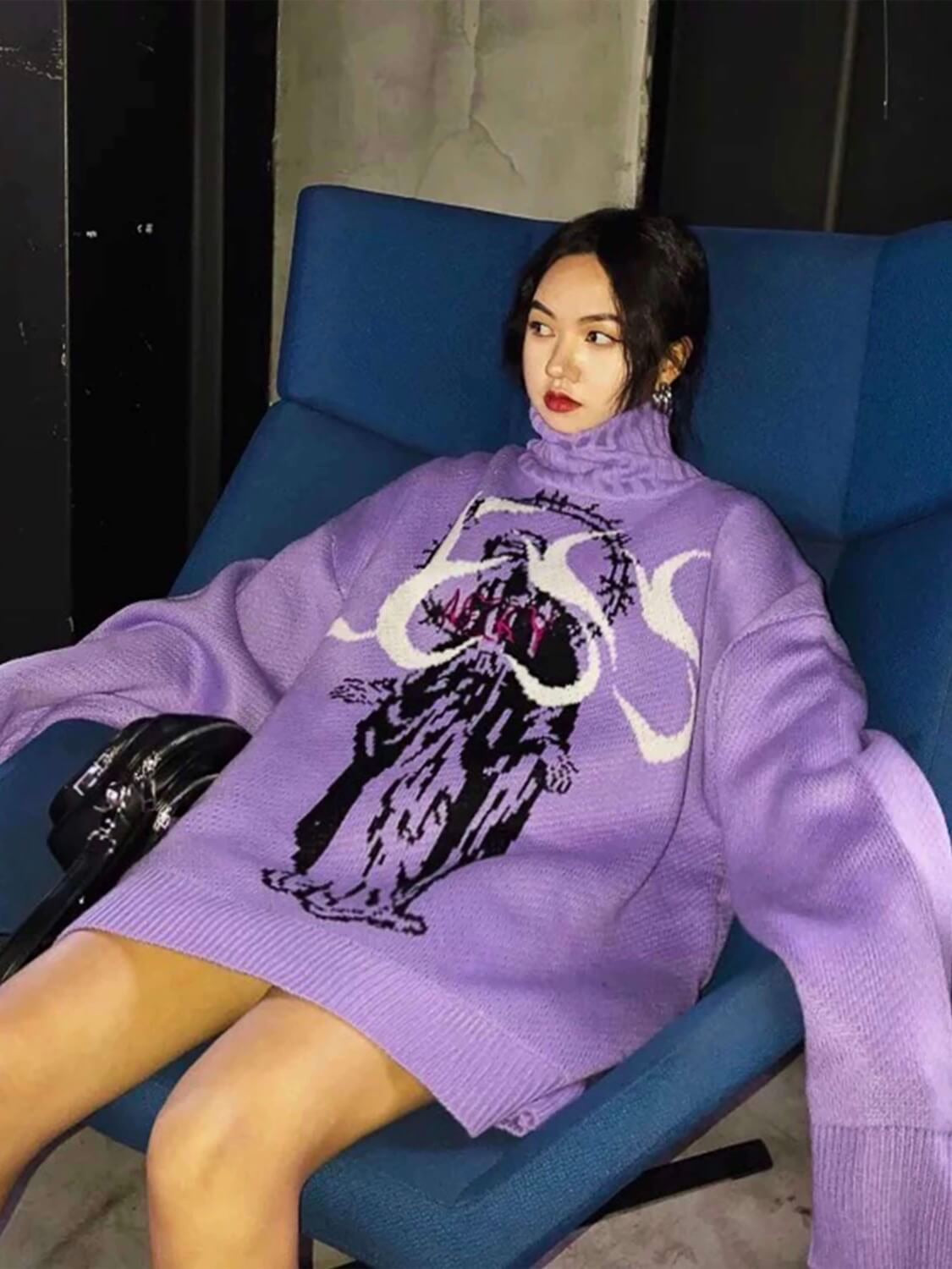 purple knitted sweater with the Virgin Mary in black and her head is surrounded by a large crown of barbed wire. A red inscription is sewn on his chest and the white word "LESS" occupies all the space available on the chest worn