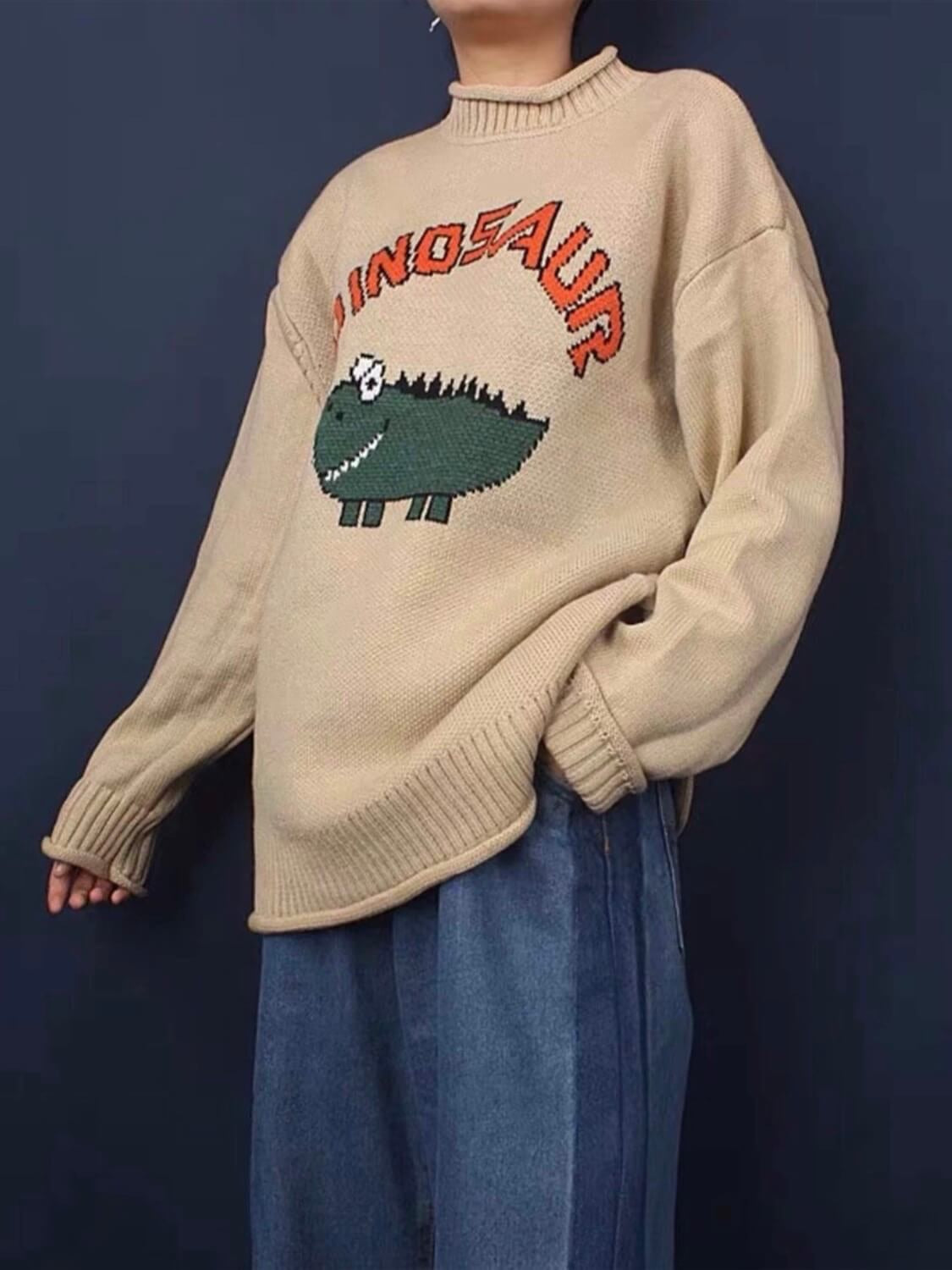 beige knitted sweater with a dinosaur drawn by a child with dinosaur written in orange above the dinosaur