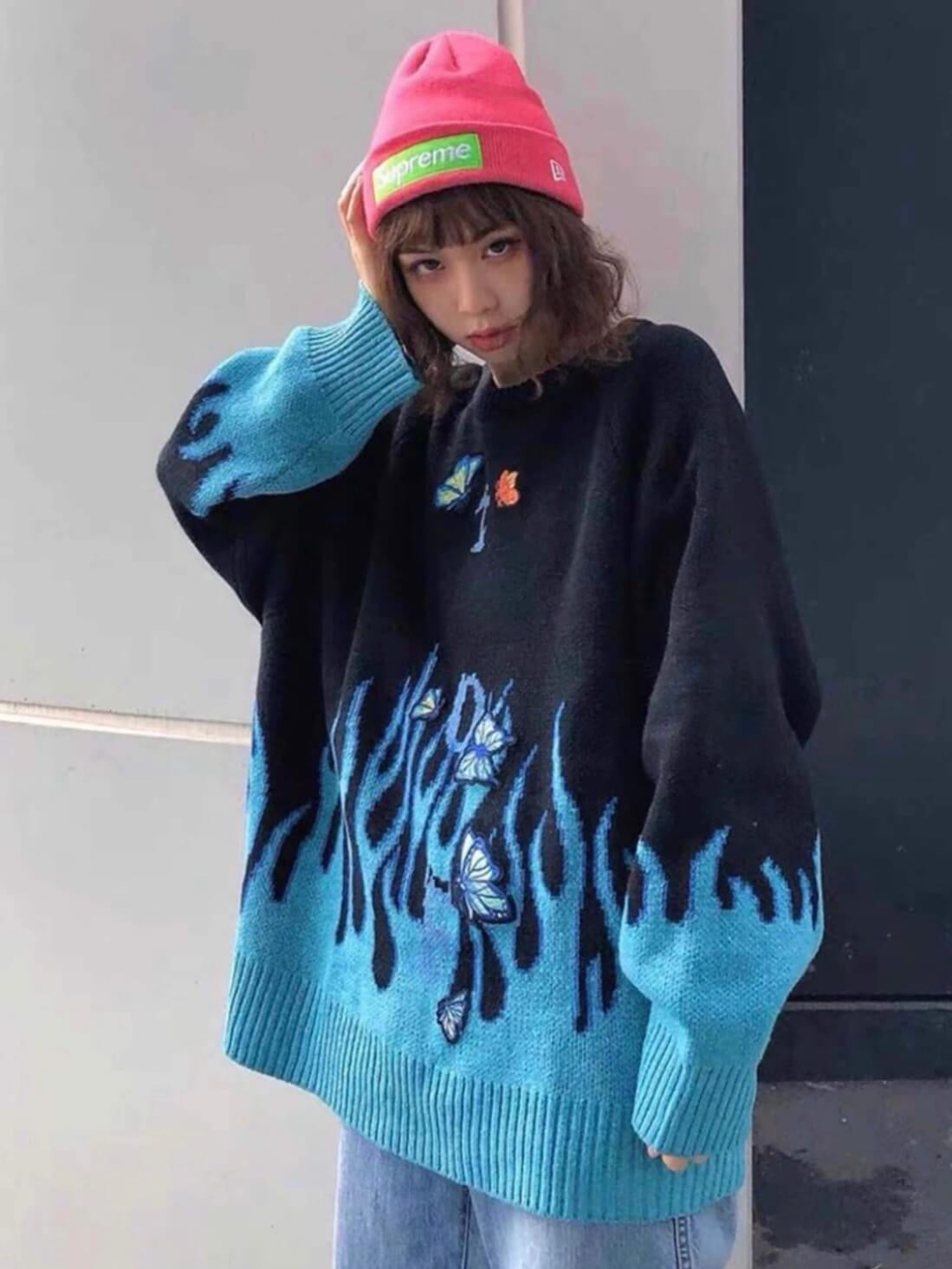 black knitted sweater with blue flames that comes from the bottom of the sweater and the wrists with blue embroidered butterflies worn