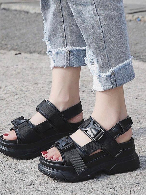 black faux leather sandal with small platform sole, streetwear style with two elastic strap with plastic buckle covering two straps that goes above the foot worn