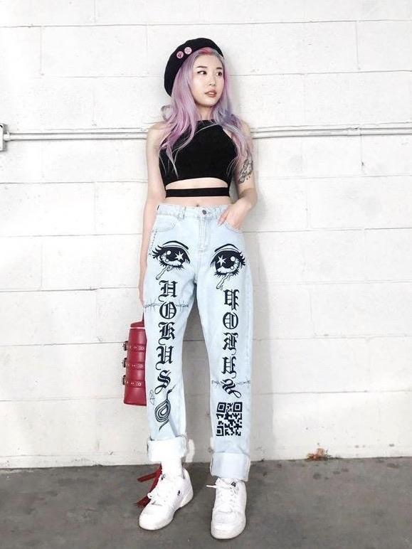 light blue jeans with two eyes at the top of the thighs, with gothic letters on the legs and snake, pentagram and qr code symbols in black worn by an asian woman