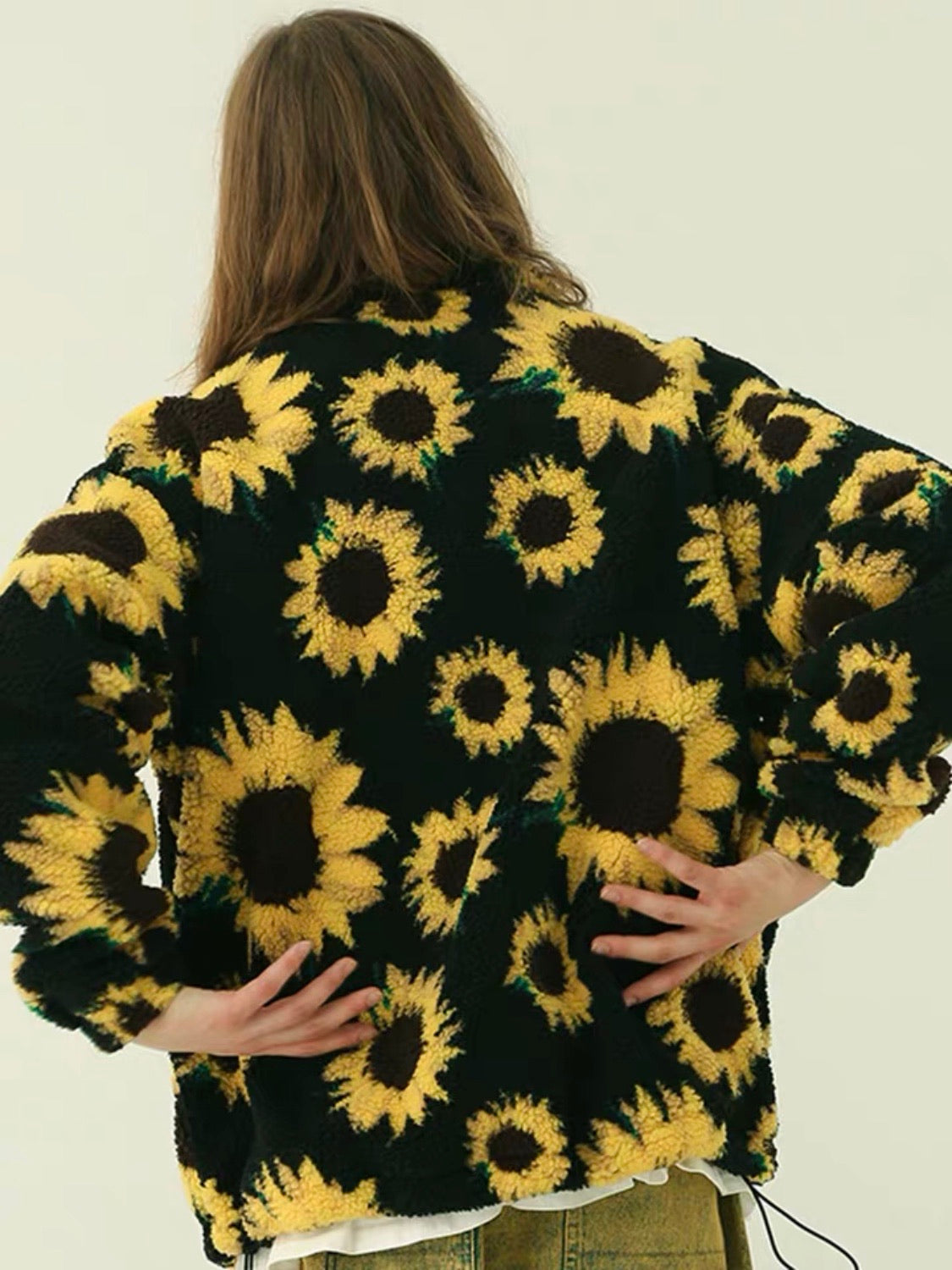 back view of our warm jacket with two front pockets and sunflowers printed on a plain black background that closes with a black zipper and adjustable by an elastic at the waist