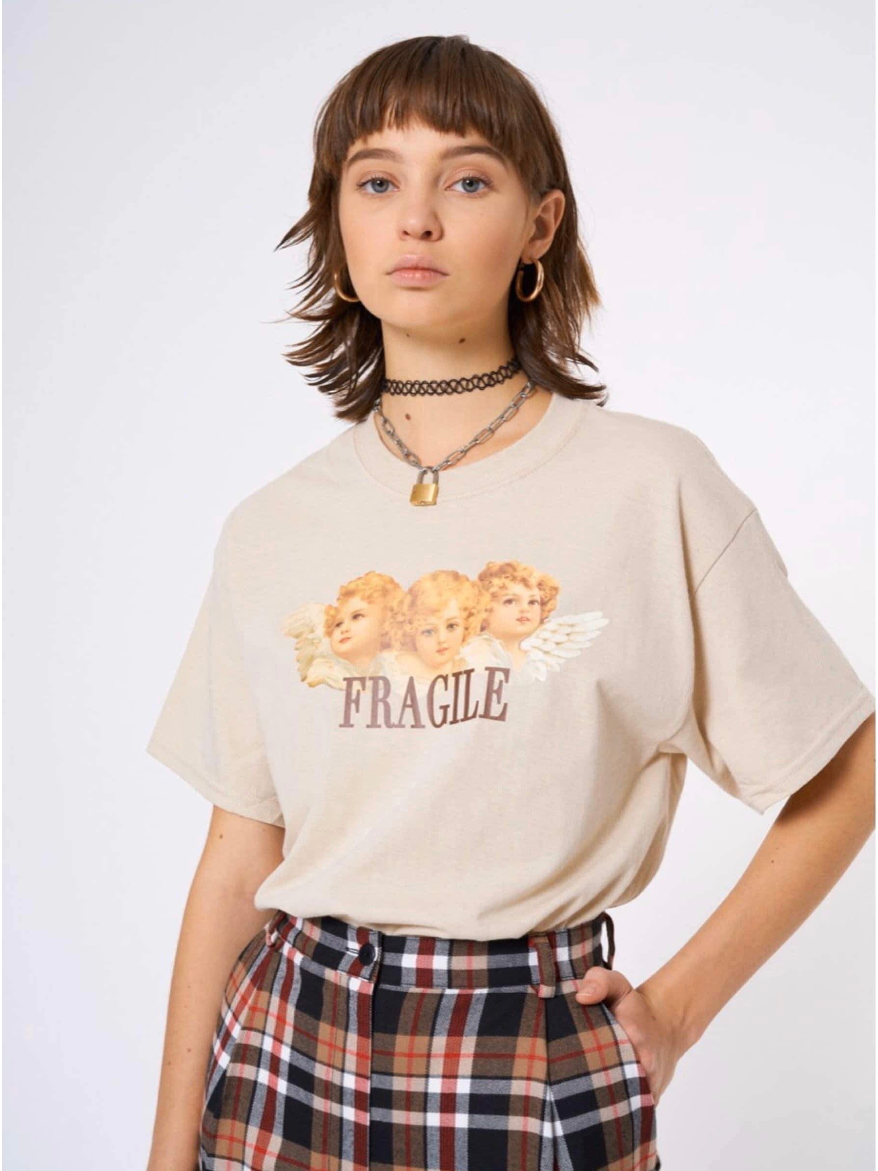 beige tshirt with three angels printed on the front with the text below fragile in brown