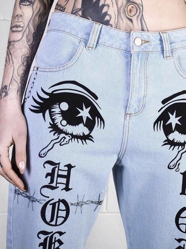 details of our light blue jeans with two crying eyes at the top of the thighs, with gothic letters on the legs and snake, pentagram and qr code symbols in black